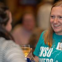 woman in GVSU Lakers t-shirt holding a drink talks to another person at celebration event